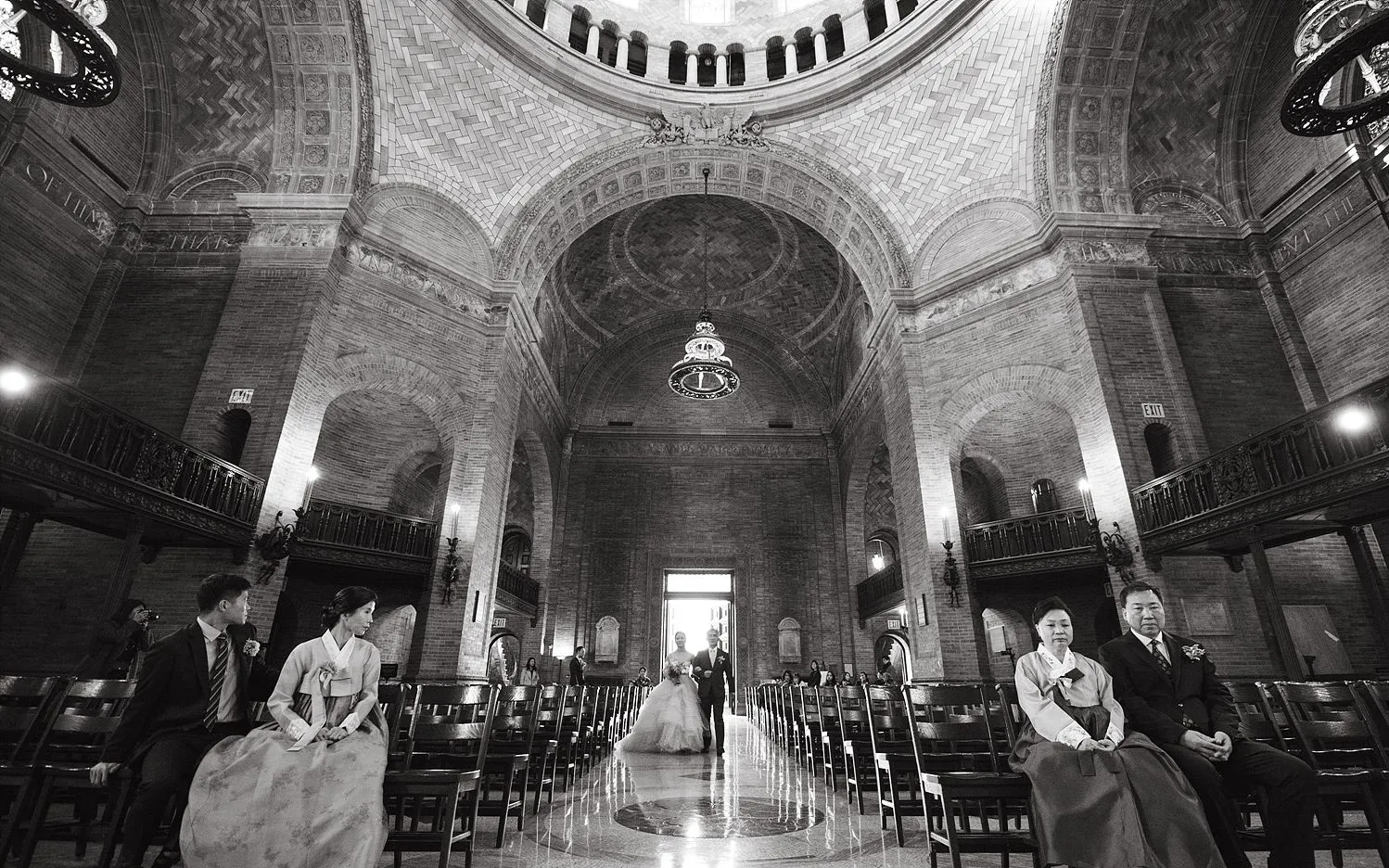 Two sets of parents sitting in the front row of the Chapel as their children walk down the aisle. 